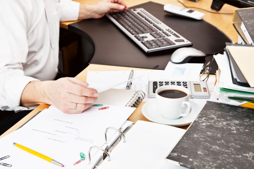 Mann Multitasking im Büro mit einer Tasse Kaffee, einem Planer und Computer