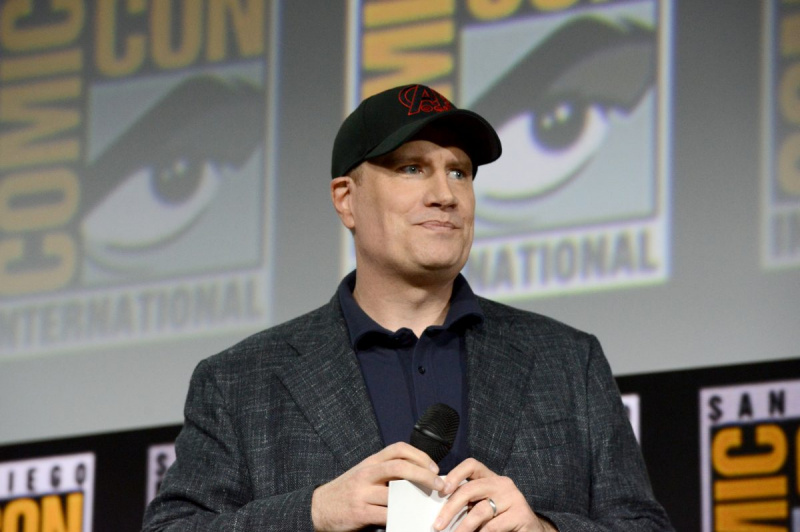   El presidente de Marvel Studios, Kevin Feige, aparece en el escenario de la Comic-Con de San Diego en 2019. Viste un traje gris oscuro sobre una camisa azul abotonada y una gorra de béisbol negra con el logo rojo de los Vengadores.