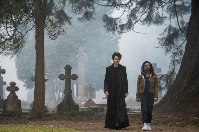   Tom Sturridge e Kyo Ra como Morpheus e Rose Walker em'The Sandman' for our review of the Netflix series. The characters are walking side by side in a graveyard.