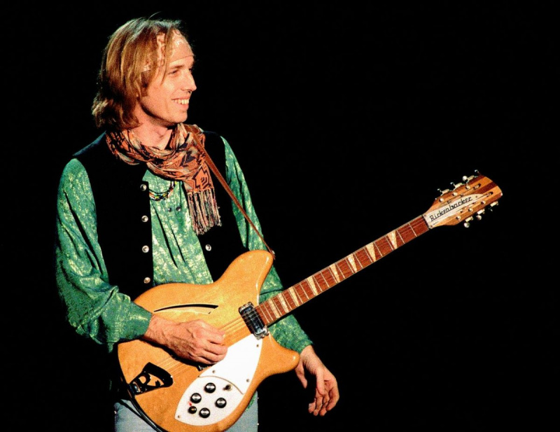   Tom Petty veste uma camisa verde e um colete e segura uma guitarra.