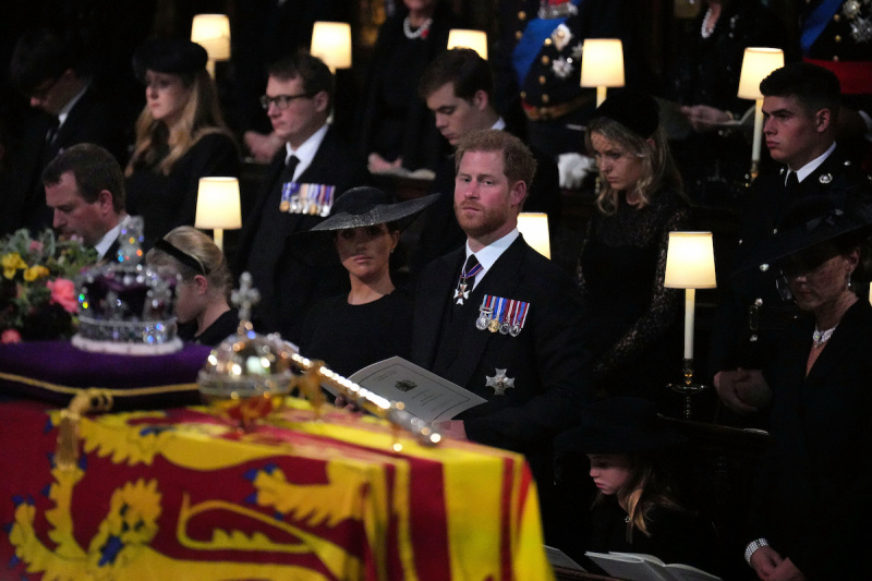   Prințul Harry și Meghan Markle, care s-au așezat în al doilea rând la Queen Elizabeth's funeral reportedly due to age order seating arrangements, stand in the front row as As Queen Elizabeth's coffin passes them at St. George's Chapel